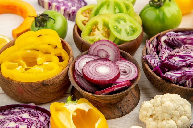 Bottom view wooden bowls with cut vegetables cauliflower onion red cabbage green tomato on white surface