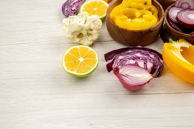 Bottom view wooden bowls with cut vegetables cauliflower onion red cabbage lemon yellow bell pepper on white surface with free place