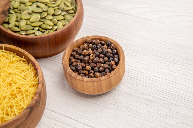 Bottom view wooden bowls with thin pasta tube black pepper pumpkin seeds on grey table free space