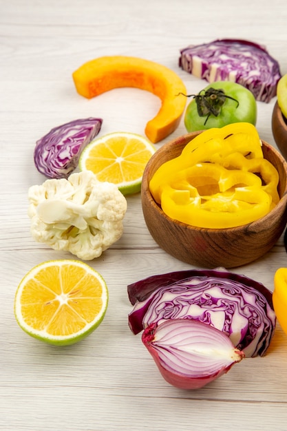 Bottom view wooden bowls with yellow bell pepper cauliflower pumpkin onion red cabbage lemon on white ground with free place