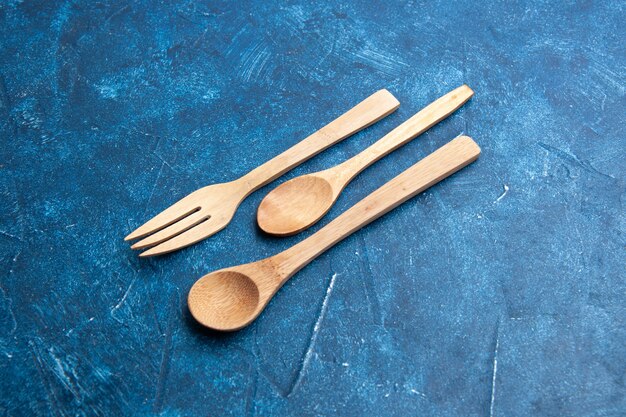 Bottom view wooden fork spoon knife on blue surface with free space