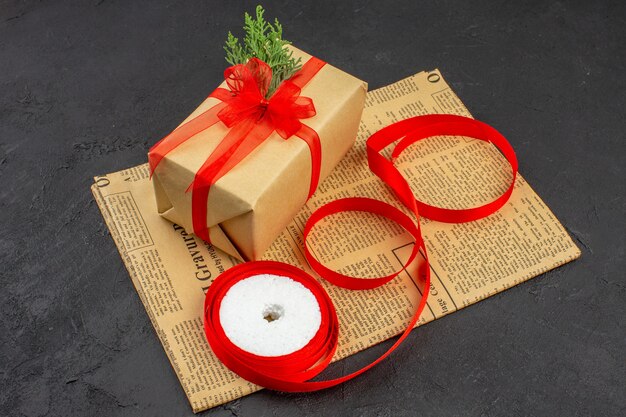 Bottom view xmas gift in brown paper branch fir ribbon on newspaper on dark