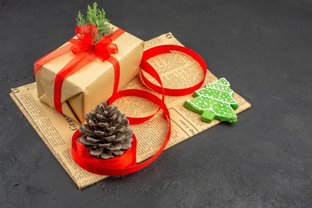 Bottom view xmas gift in brown paper branch fir ribbon on newspaper xmas ornaments on dark background xmas photo