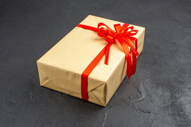 Рождественский подарок в коричневой бумаге, перевязанный красной лентой на темном фоне, свободное пространство, вид снизу