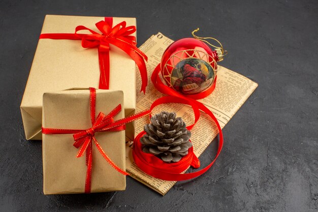 Bottom view xmas gifts in brown paper ribbon xmas tree toy on newspaper on dark background