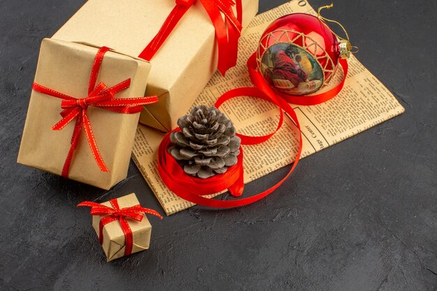 Bottom view xmas gifts in brown paper ribbon xmas tree toy on newspaper on dark background