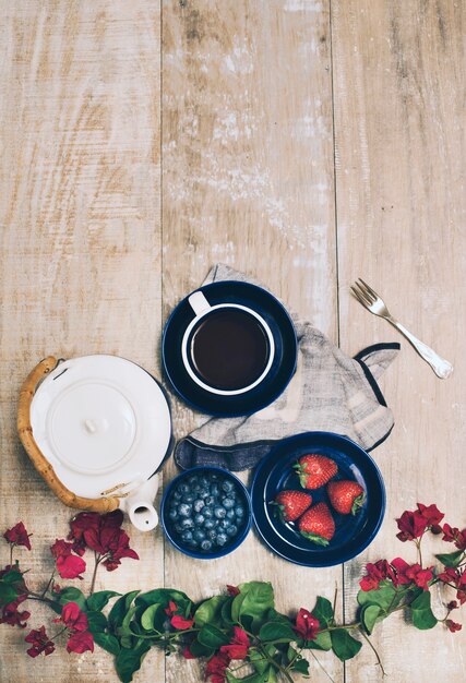 Bougainvillea pink flower; strawberries; blueberries; teapot and coffee cup on wooden table