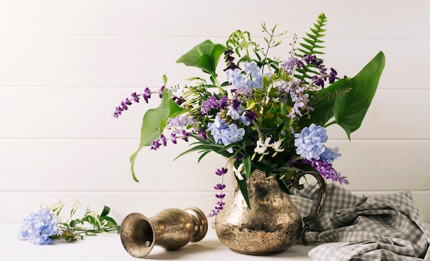 Bouquet of blooms in vase near pitcher on table