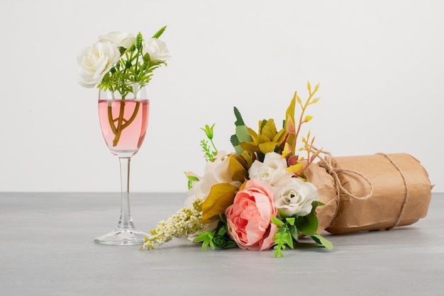 Bouquet of flowers and a glass of rose wine on grey surface.