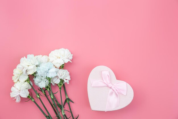 Bouquet of flowers heart shaped gift box on pink background flat lay