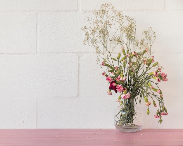 Bouquet of flowers and plant twigs in vase near wall