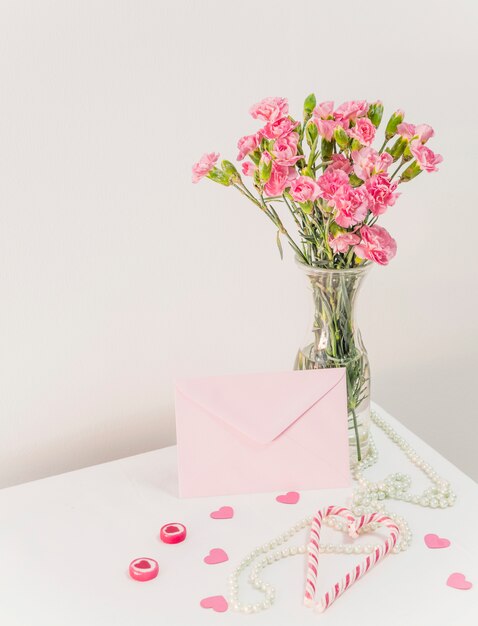 Букет цветов в вазе возле леденцы, конверт и бусы на столе