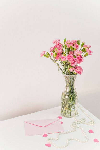 Букет цветов в вазе возле конверта, бумажные сердечки и бусы на столе