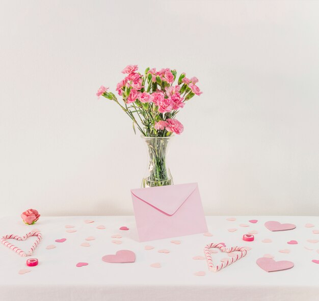 Bouquet of flowers in vase near set of paper hearts, envelope and candy canes