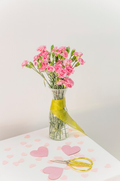 Букет цветов в вазе с лентой возле ножниц и бумажных сердечек