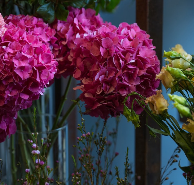 A bouquet of pink flowers with green leaves inside a vase standing on room wall