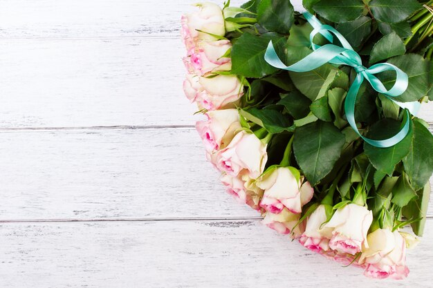 Bouquet of pink roses with blue ribbon on a vintage wooden background