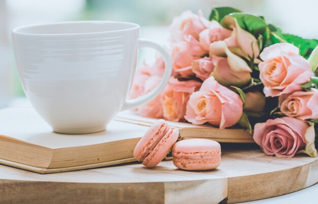 Bouquet of pink roses on a wooden board with a glass on top of the book and macaroon cookies