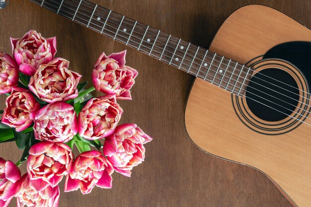 木製の背景上のピンクのチューリップとアコースティックギターの花束
