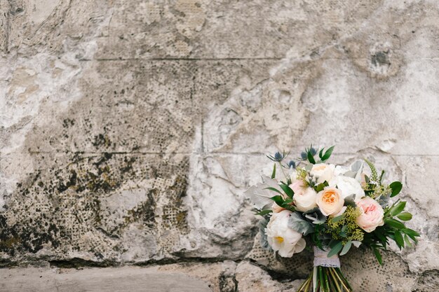 Bouquet of pink and white poenies lies before a concrete wall