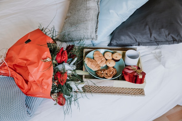 Bouquet and present near breakfast on bed