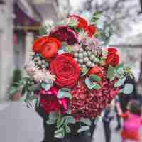 Free photo a bouquet of red roses, peonies and green decorative flowers with leaves