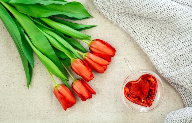 Букет красных тюльпанов и чашка в форме сердца с видом сверху на красный чай