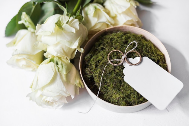 Bouquet of roses and bowl of moss and wedding rings with blank tag