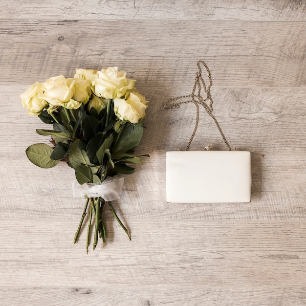 Free photo bouquet of roses tied with white ribbon with clutch on wooden backdrop