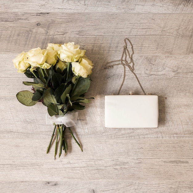 Bouquet of roses tied with white ribbon with clutch on wooden backdrop
