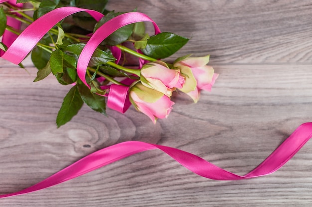 Bouquet of roses with pink ribbon on wood