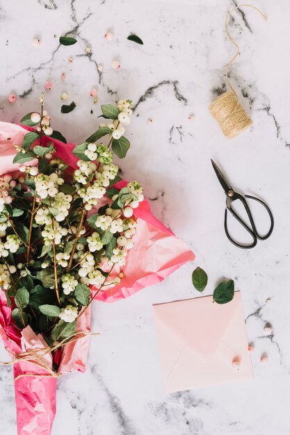 symphoricarpos albusの花束;はさみでピンクの紙に包まれた一般的な雪の小枝。スプールと封筒