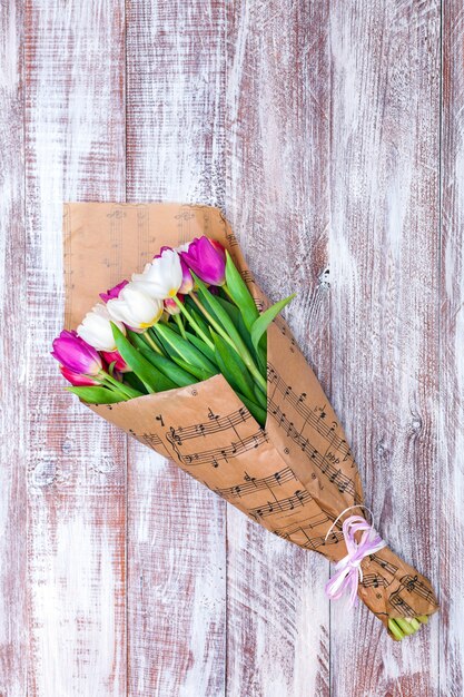 The bouquet of tulips is wrapped in a paper isolated on a wood background