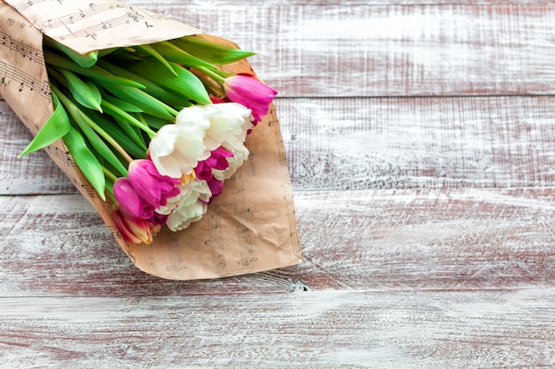 The bouquet of tulips is wrapped in a paper isolated on a wood background