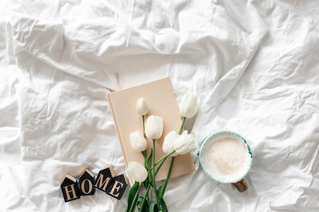 Free photo a bouquet of white tulips a cup of coffee and a book in a white bed top view