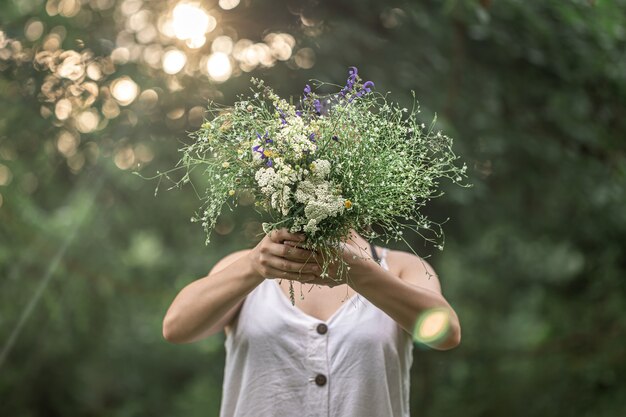 Букет полевых цветов в руках девушки в лесу.