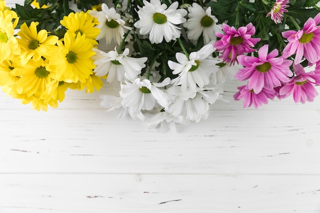 黄色のブーケ。白い木製の織り目加工の背景に白とピンクのデイジーの花