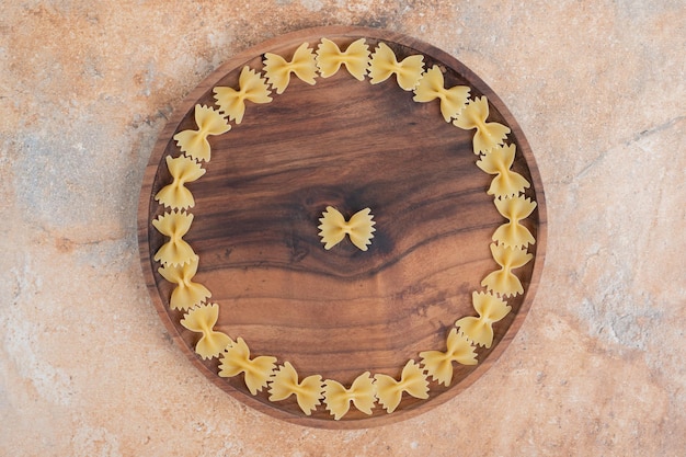 Макаронные изделия с галстуком-бабочкой на деревянной тарелке на мраморном пространстве.