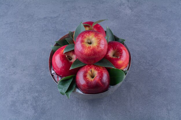 A bowl of apples with leaves on the dark surface