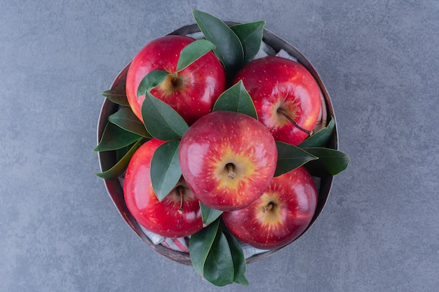 A bowl of apples with leaves on marble table.