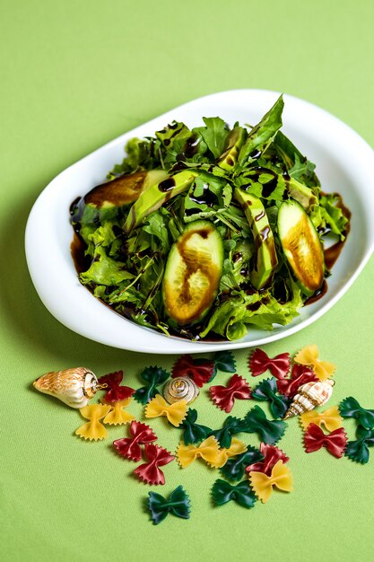 A bowl of avocado salad with cucumber, spinach, lettuce with sauce on top