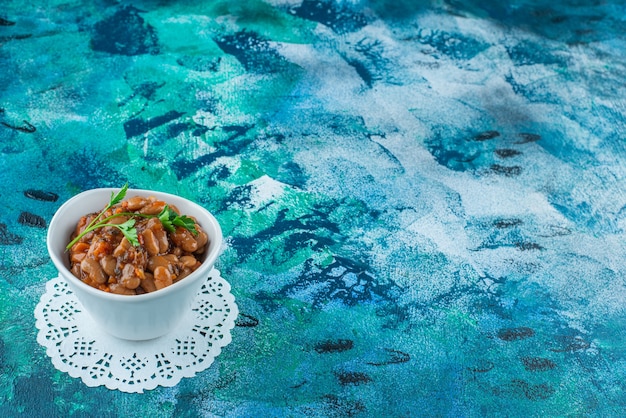 A bowl of baked beans on a coaster, on the blue background. 