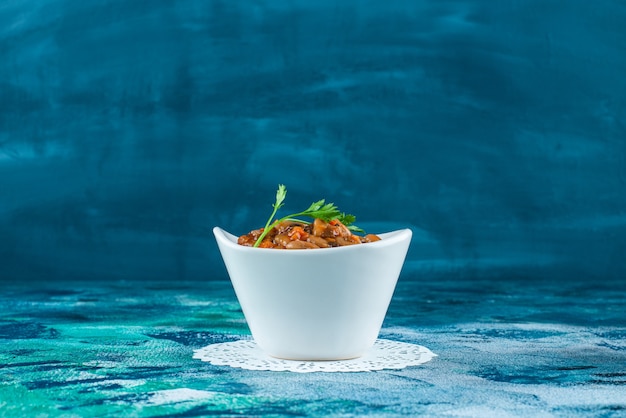 A bowl of baked beans on a coaster, on the blue table. 