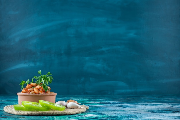 Free photo bowl of baked beans, garlic and pepper on trivet on blue.