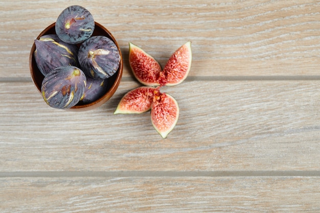 A bowl of black figs and slices of figs on a wooden table