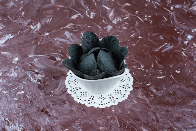 A bowl of black potato chips on a coaster , on the marble table. 