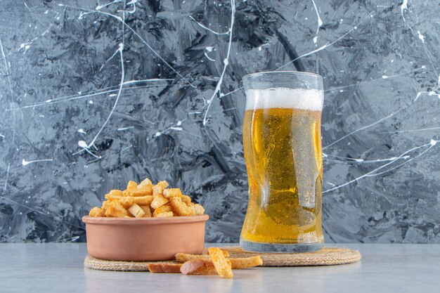 A bowl of breadcrumbs and beer in a glass on a trivet, on the marble background.