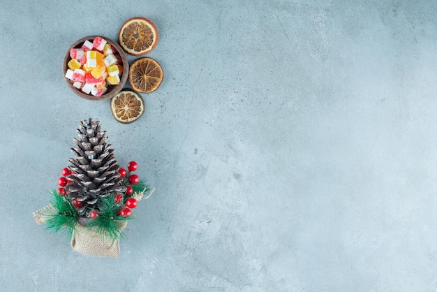 Bowl of candies, dried lemon slices and a christmas decoration on marble.