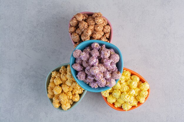 A bowl of caramel coated popcorn with two sliced pieces of lemon next to a bundle of puffy flowers on marble.