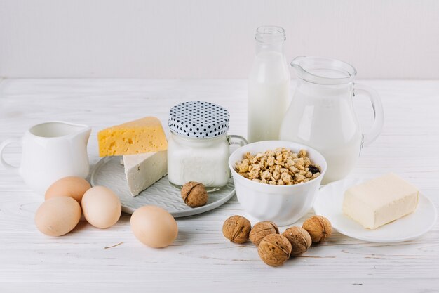 Bowl of cereals; milk; eggs; cheese and walnuts on white textured backdrop